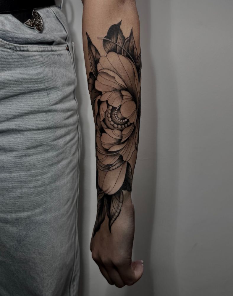 Tatuagem de peônia com folhas cobrindo o antebraço.