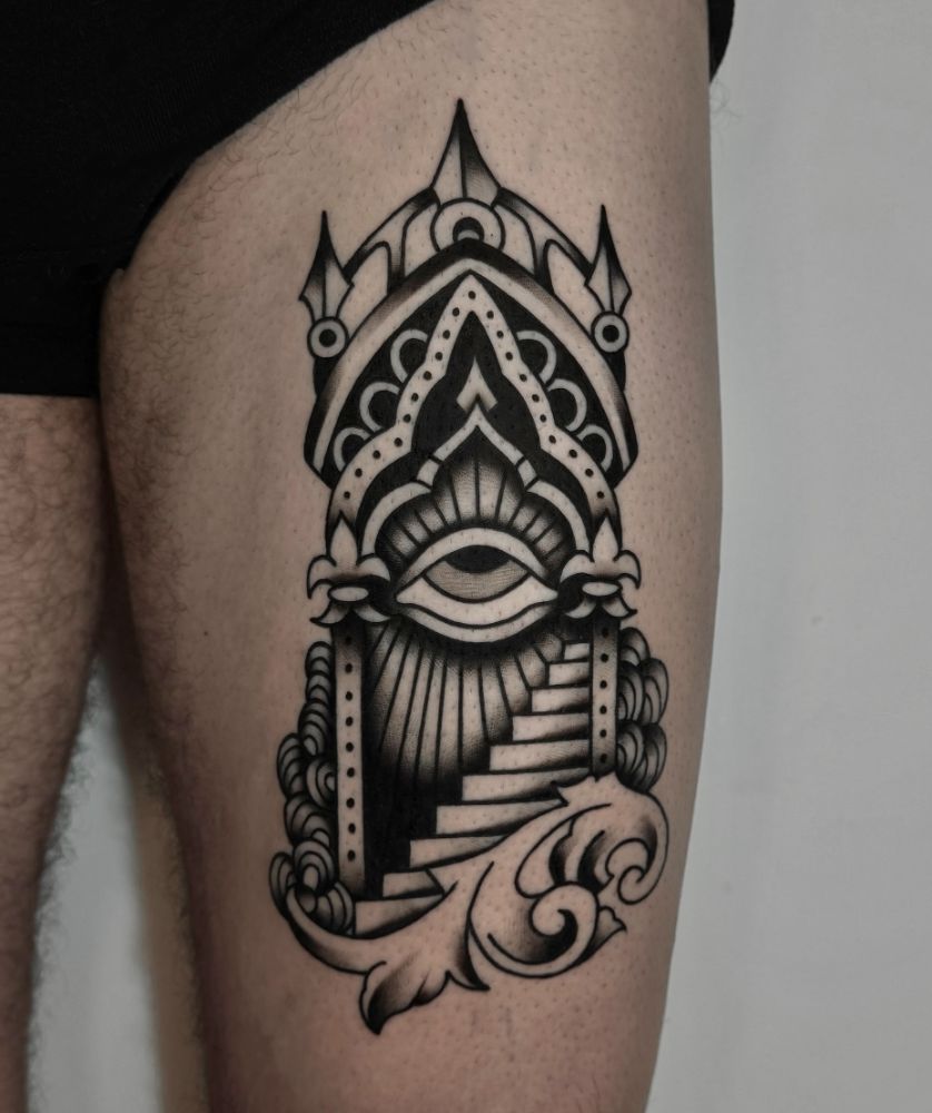 Tatuagem de olho dentro de arco ornamental, na coxa.