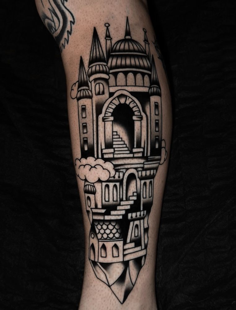 Tatuagem de castelo com torres e escadaria, na panturrilha.