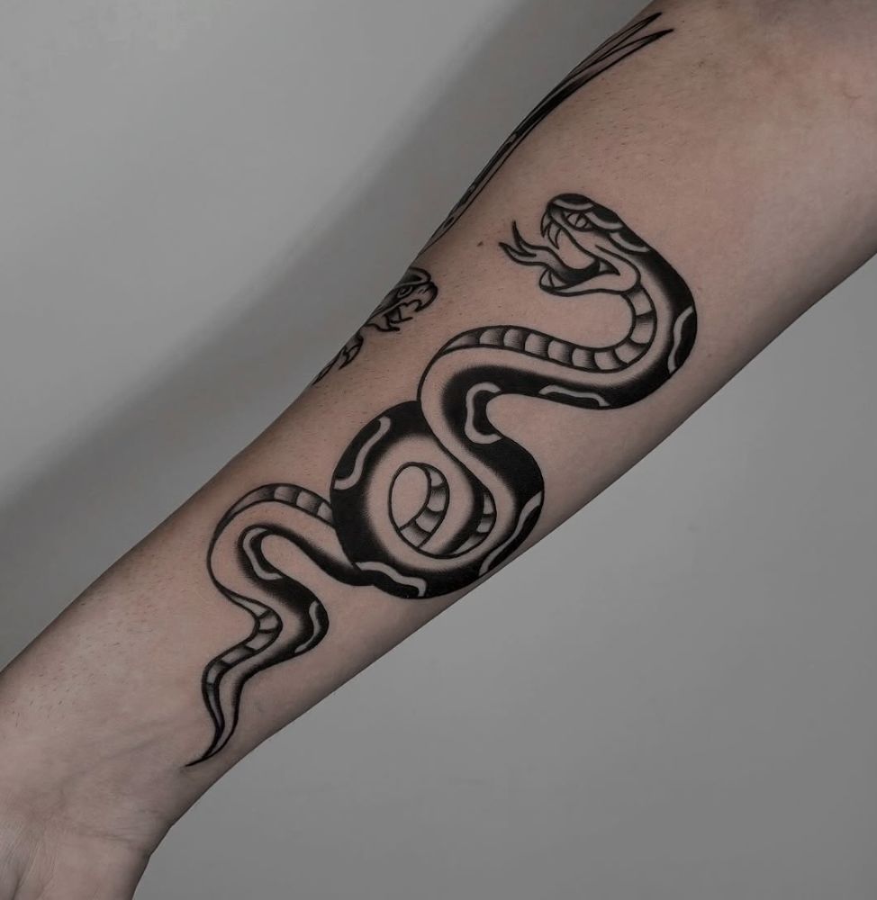 Tatuagem old school de serpente em preto sólido, no antebraço.