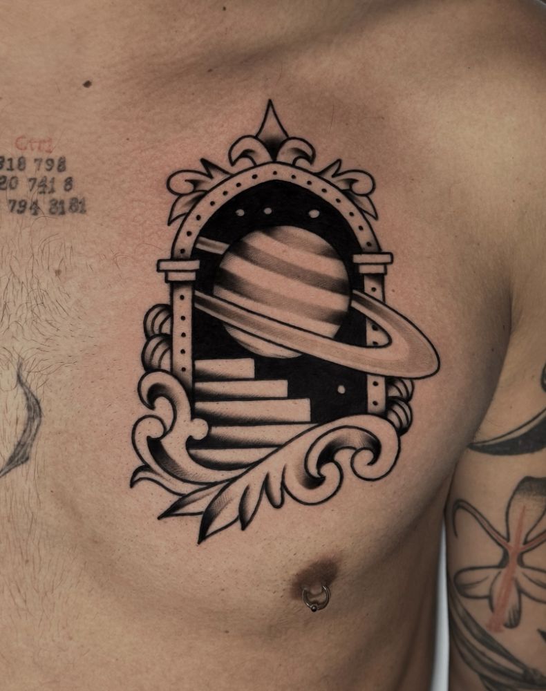 Tatuagem de arco ornamental com o planeta Saturno, no peito.